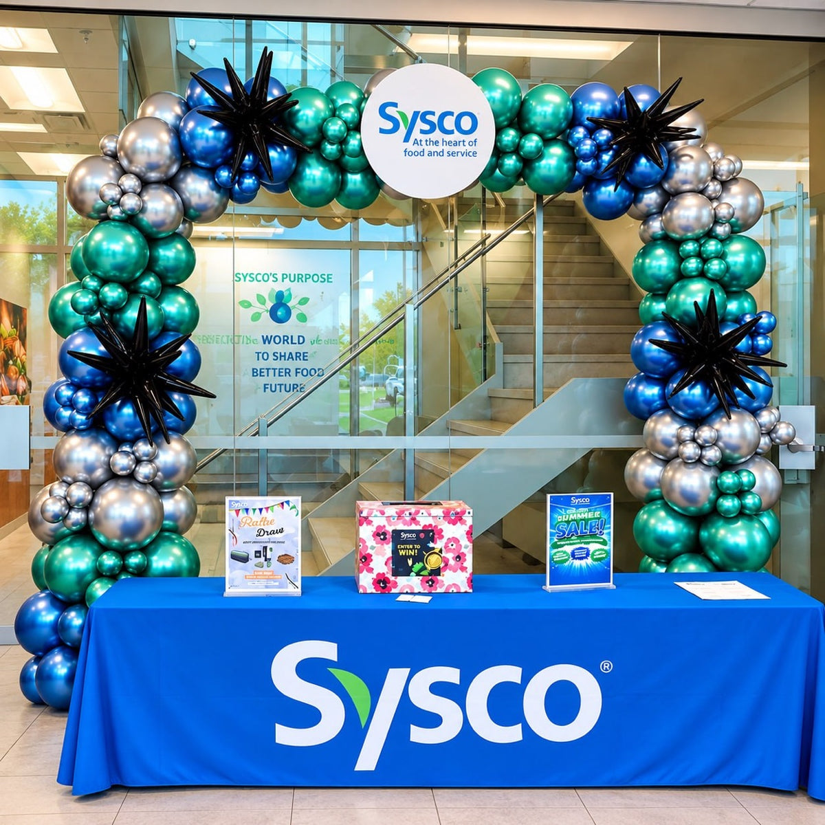 Chrome organic balloon arch / garland in teal, blue and silver with starbursts and a Sysco logo sign over a registration table