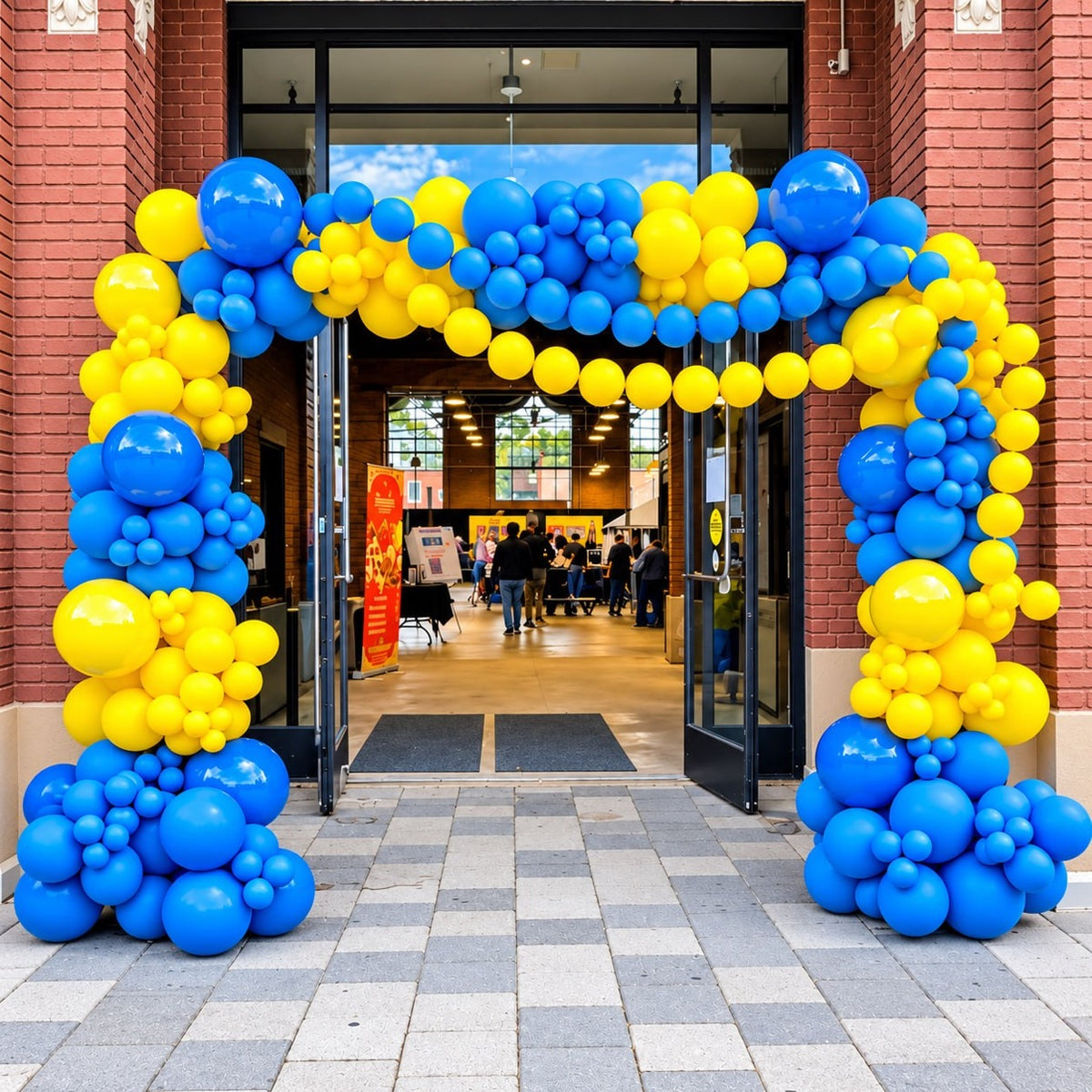 Organic balloon arch / garland in blue and yellow framing a brick building entrance
