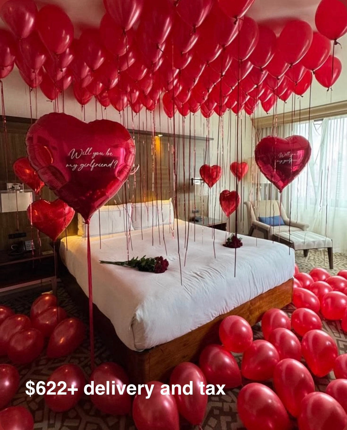 Romantic hotel room proposal setup with red helium balloons on the ceiling, giant red heart foil balloons with Will you be my girlfriend inscription and roses on the bed