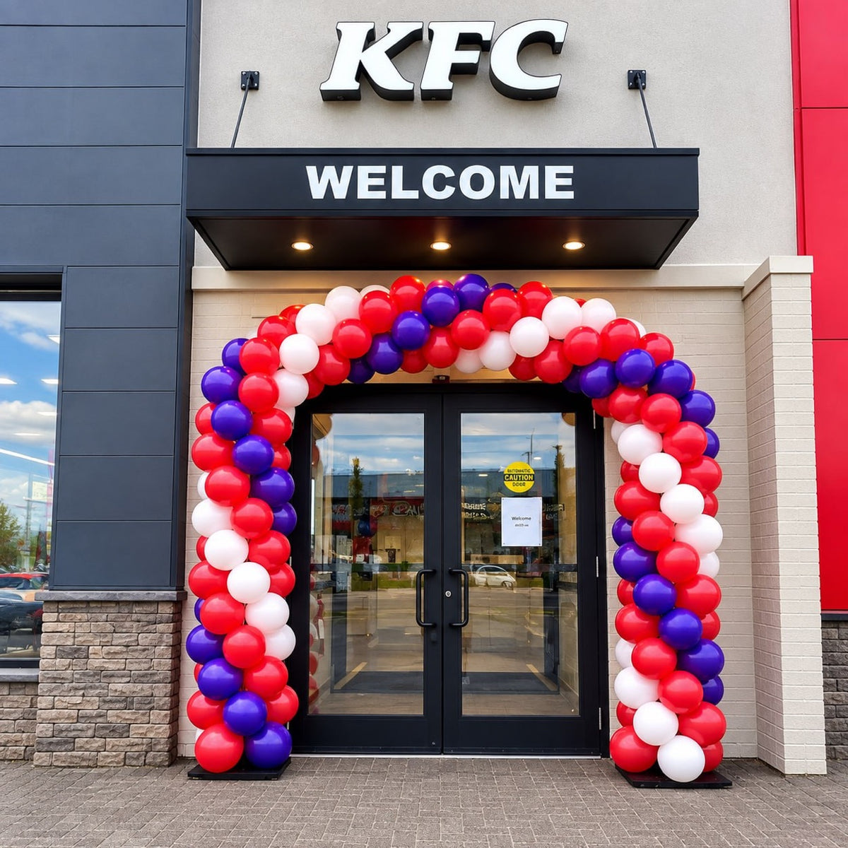 Classic spiral balloon arch in red, white and purple framing a KFC store entrance under a WELCOME sign
