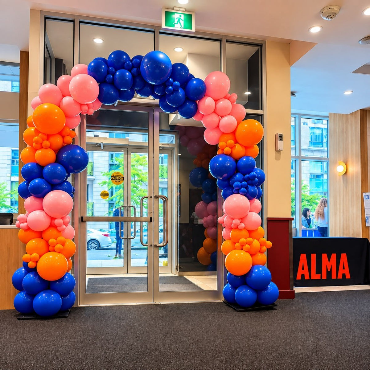 Organic balloon arch / garland in pink, orange and blue framing a glass entrance door