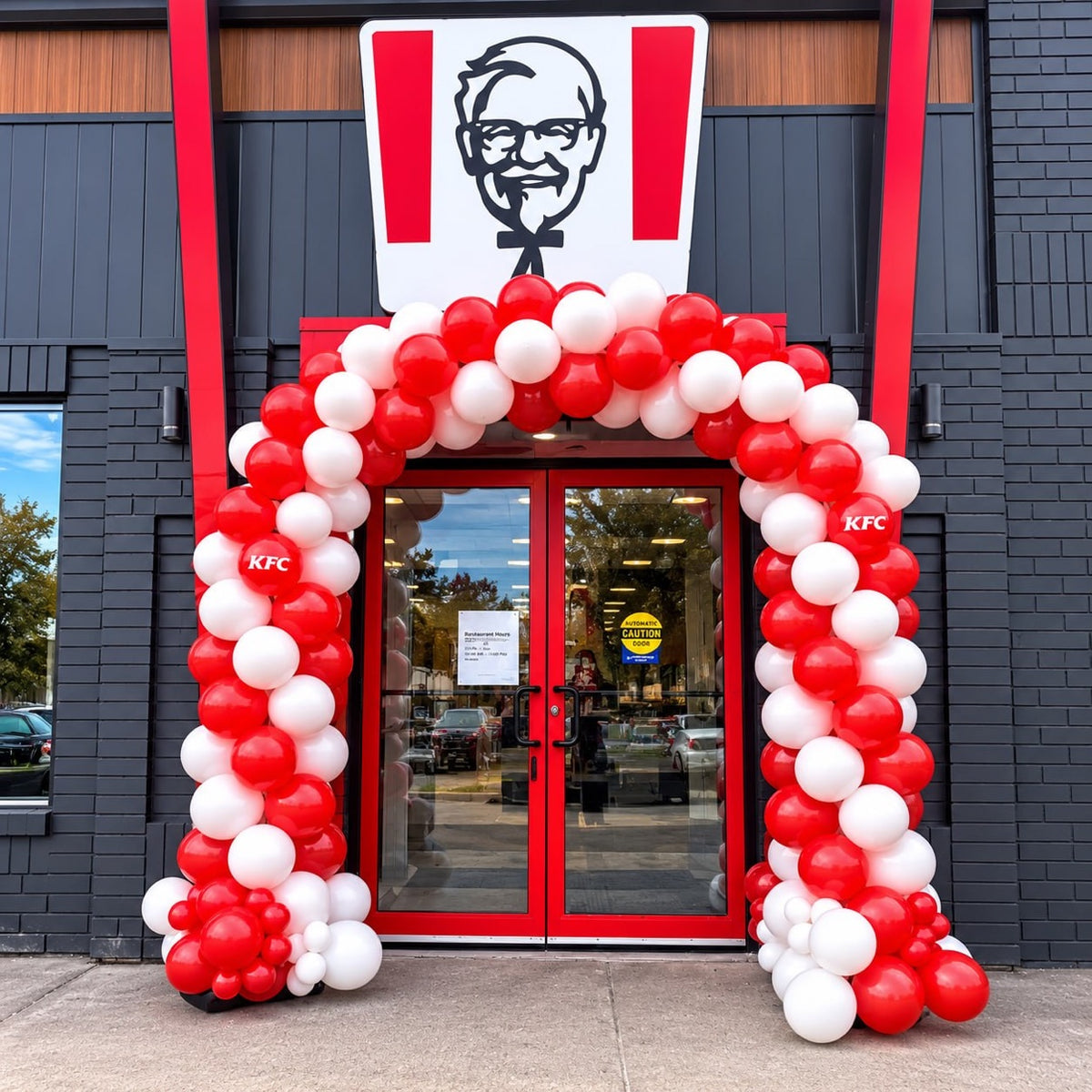 Classic spiral balloon arch in red and white with KFC logo balloons framing a KFC store entrance