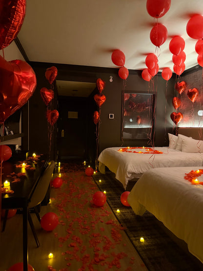 Romantic room setup with red balloons floating on the ceiling, I LOVE YOU letters, rose petal trail and LED candles on the floor