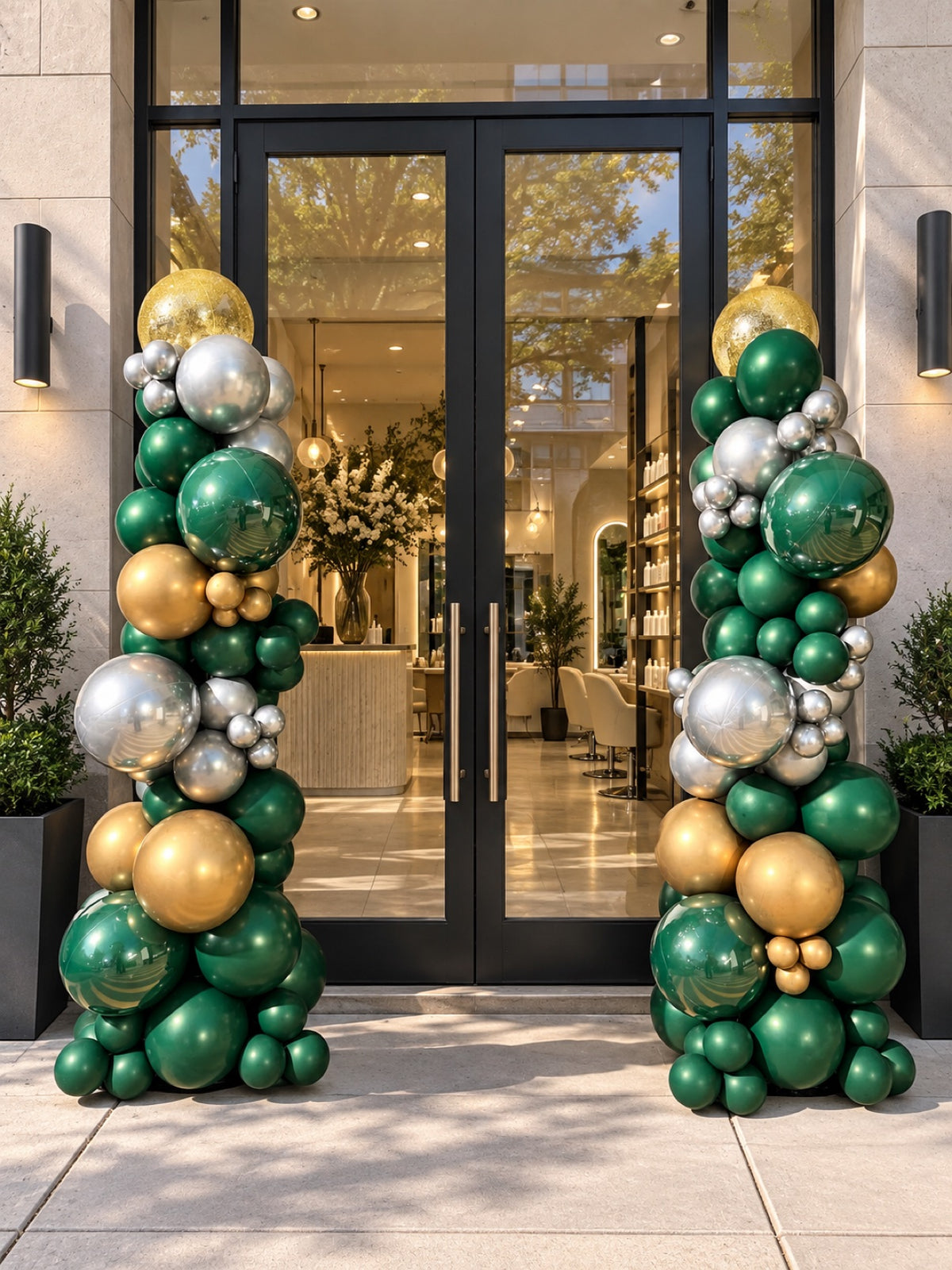 Two organic balloon columns in emerald green, metallic gold and silver flanking a glass storefront entrance