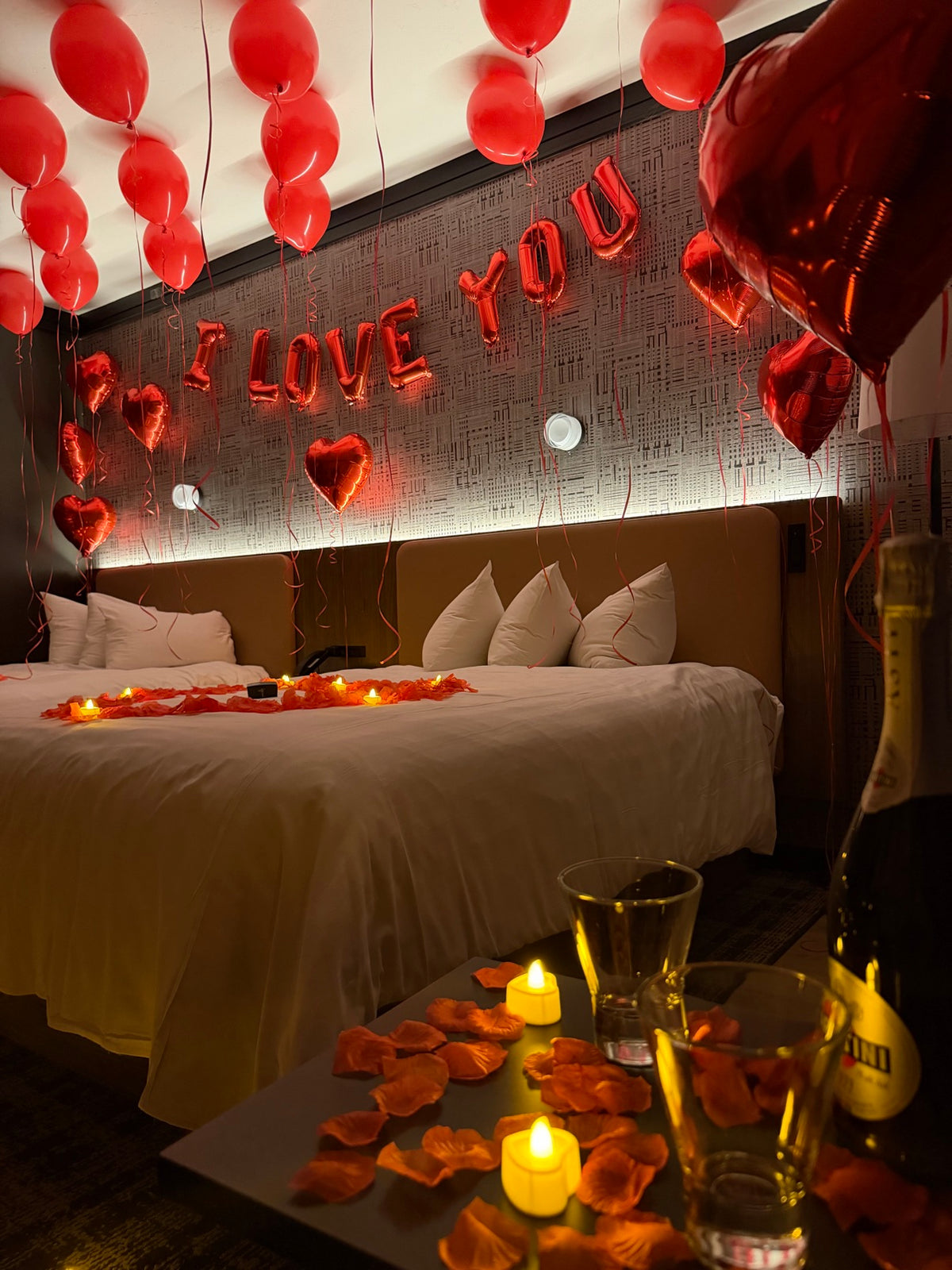 Close-up of romantic bed decor with I LOVE YOU balloons, rose petals, candles and champagne glasses on the table