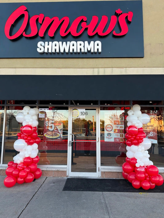 Red and white organic balloon columns at a storefront entrance
