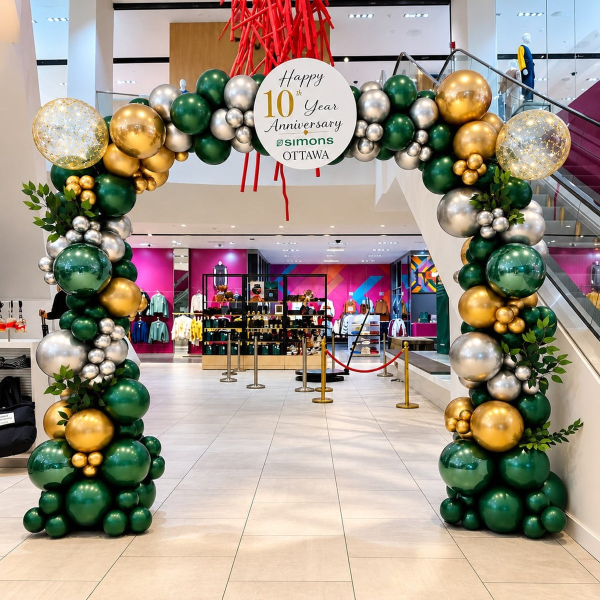 Luxury organic balloon arch / garland in emerald green, gold and silver with greenery and a Happy 10th Year Anniversary Simons Ottawa sign