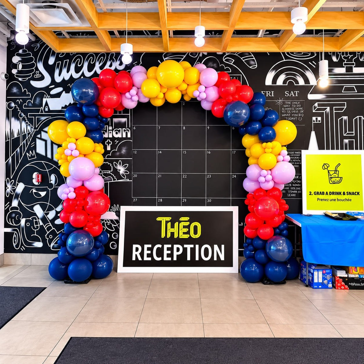 Multicolor organic balloon arch / garland in red, yellow, pink and navy framing a THÉO RECEPTION sign