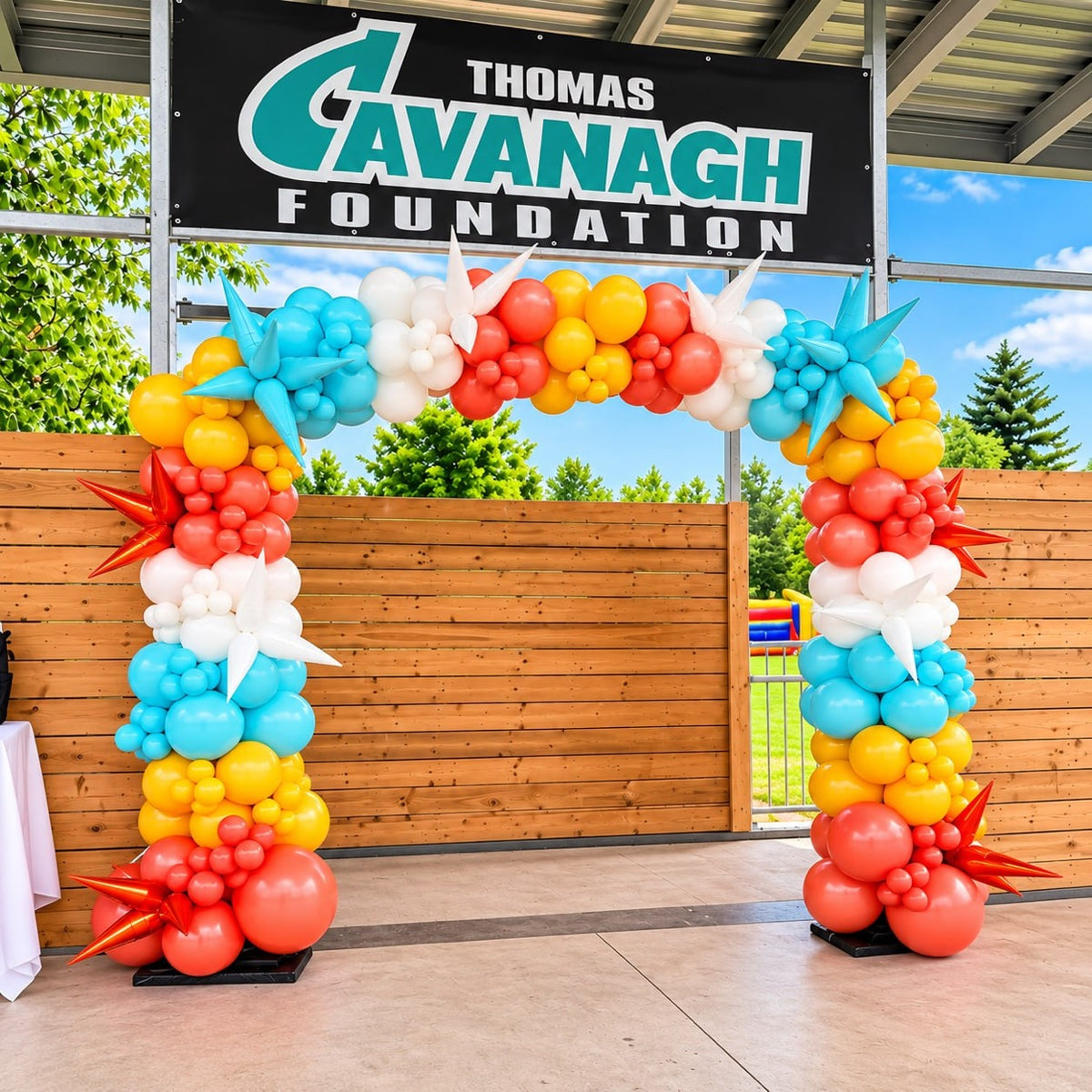 Colorful organic balloon arch / garland with starburst accents in turquoise, yellow, coral and white under a Thomas Cavanagh Foundation banner