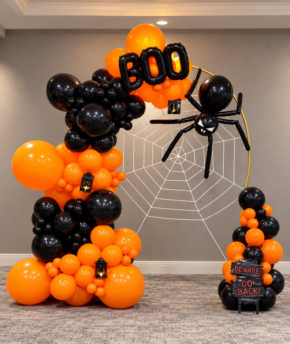 Orange and black Halloween balloon arch with BOO foil letters, balloon spider on spider web, lanterns and Beware sign