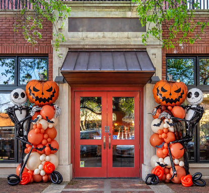 Halloween balloon columns with pumpkin and skeleton foil balloons, orange ivory and black, at a storefront entrance