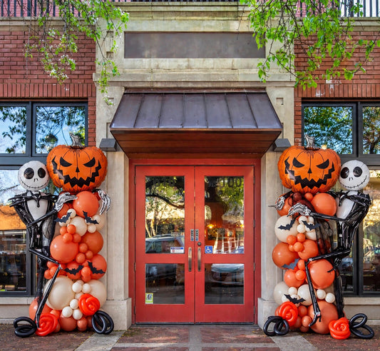 Halloween balloon columns with pumpkin and skeleton foil balloons, orange ivory and black, at a storefront entrance