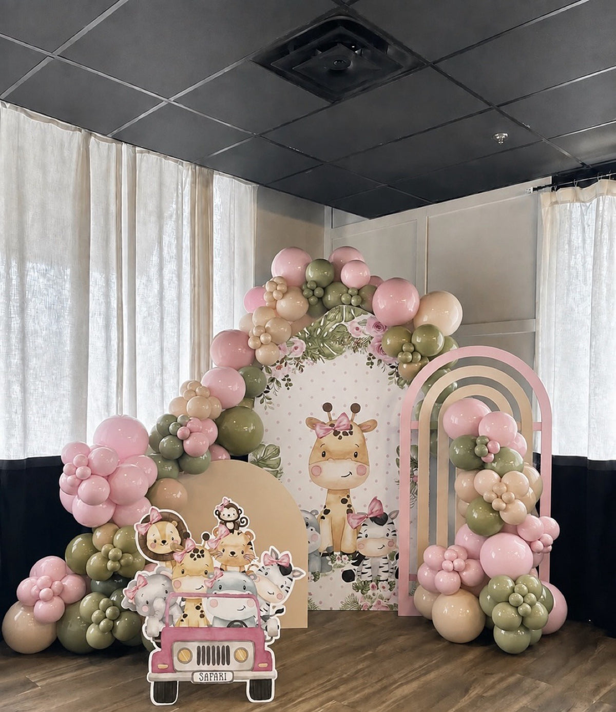 Safari giraffe balloon backdrop with printed animal panel, large blush pink and sage garland, pink rainbow arch and safari jeep cutout